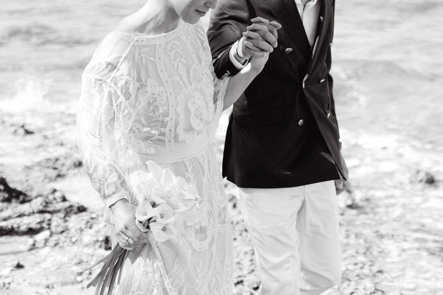 a black and white close-up photo of a man's and a woman's hands being held, the man is dressed with a black suit and white pants