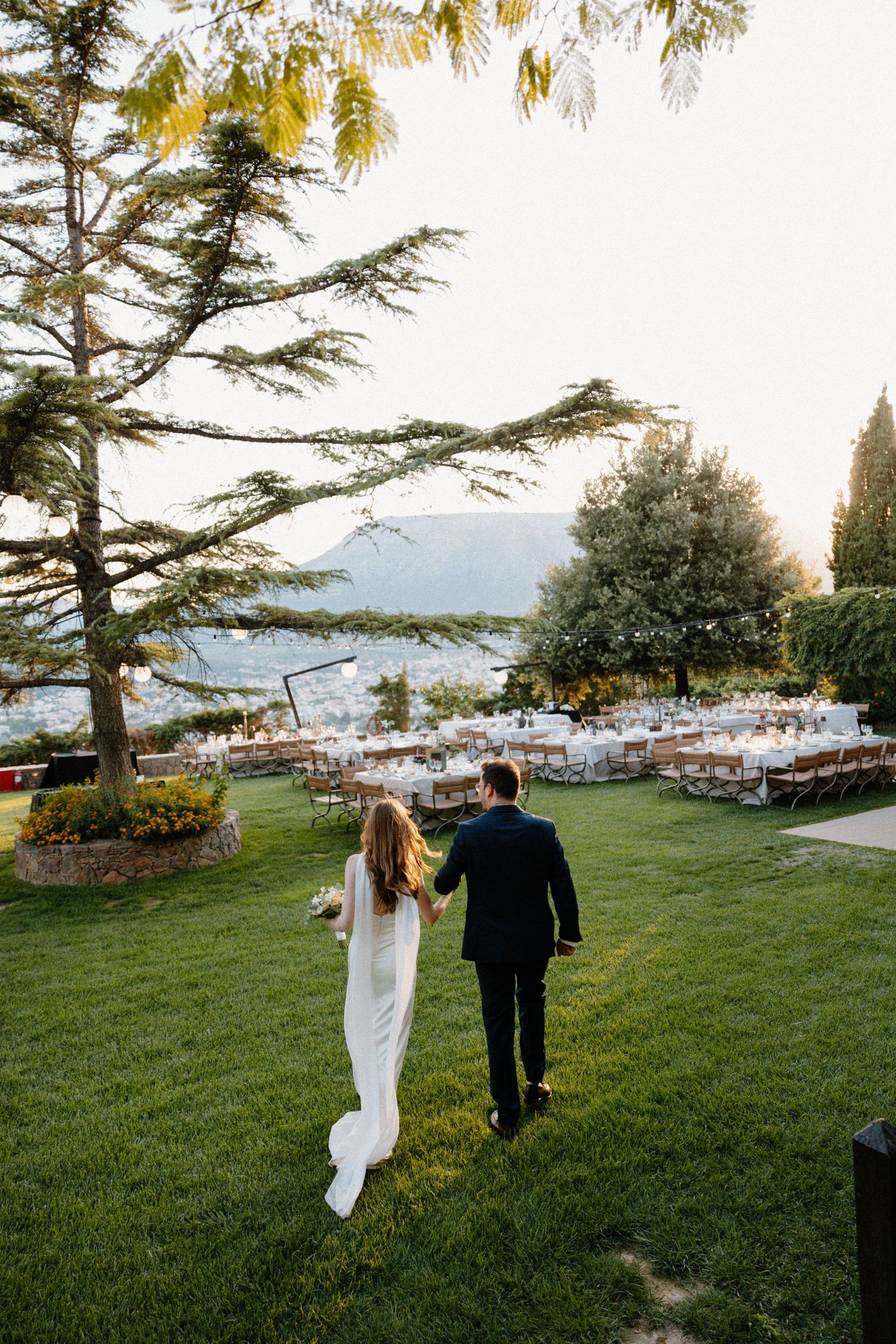 a bride and groom holding hands as they are walking into their Athens wedding venue reception table area in a lush greenery background
