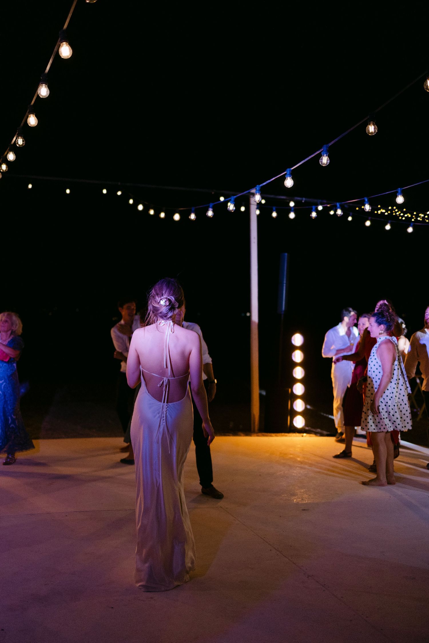 a party photo of a wedding in Spetses, Greece, showing the back of the bride dancing under coloured lights