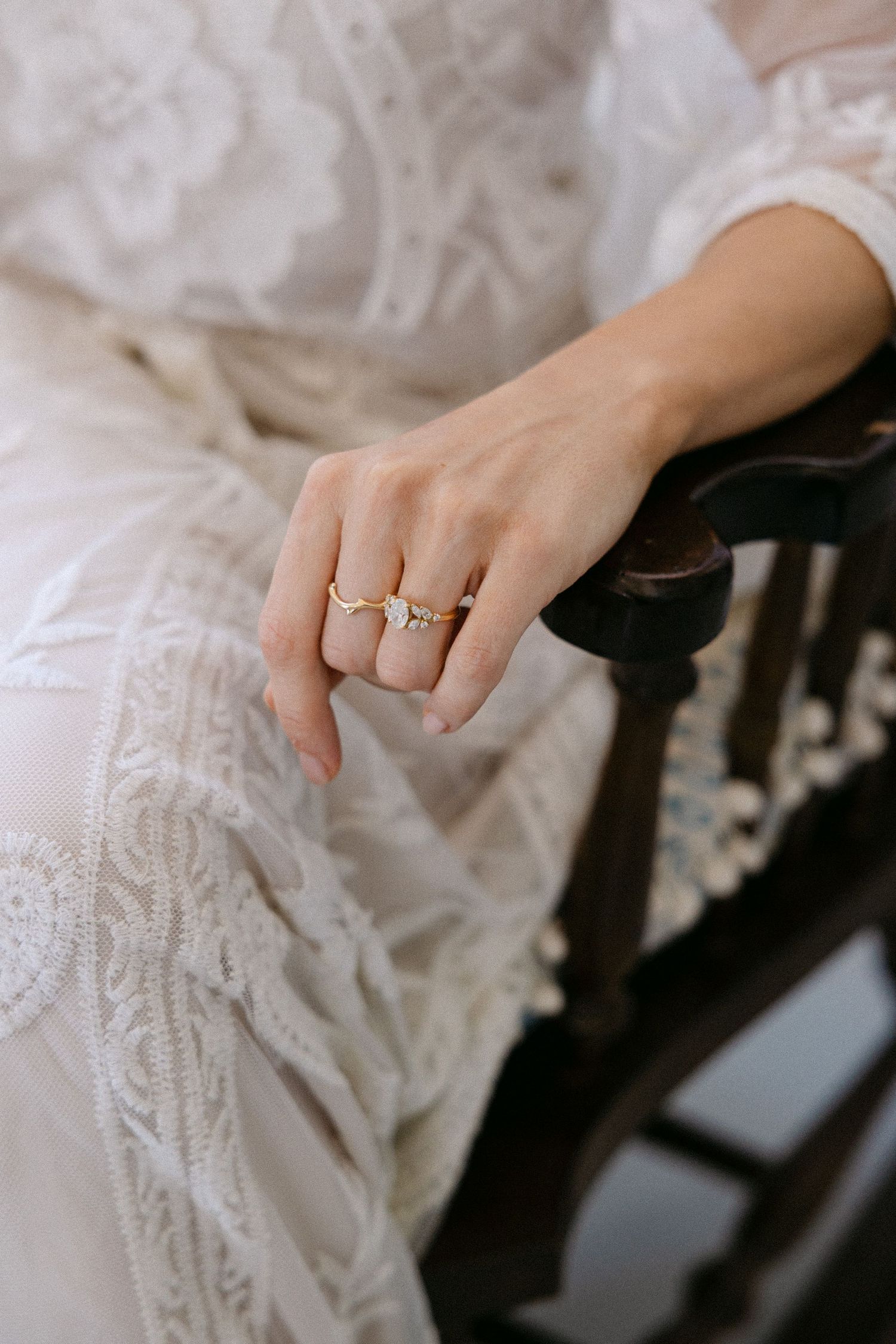 a close-up of a hand rested on a wooden armchair, wearing two gold rings  - the person appears to be wearing a lace vintage wedding dress