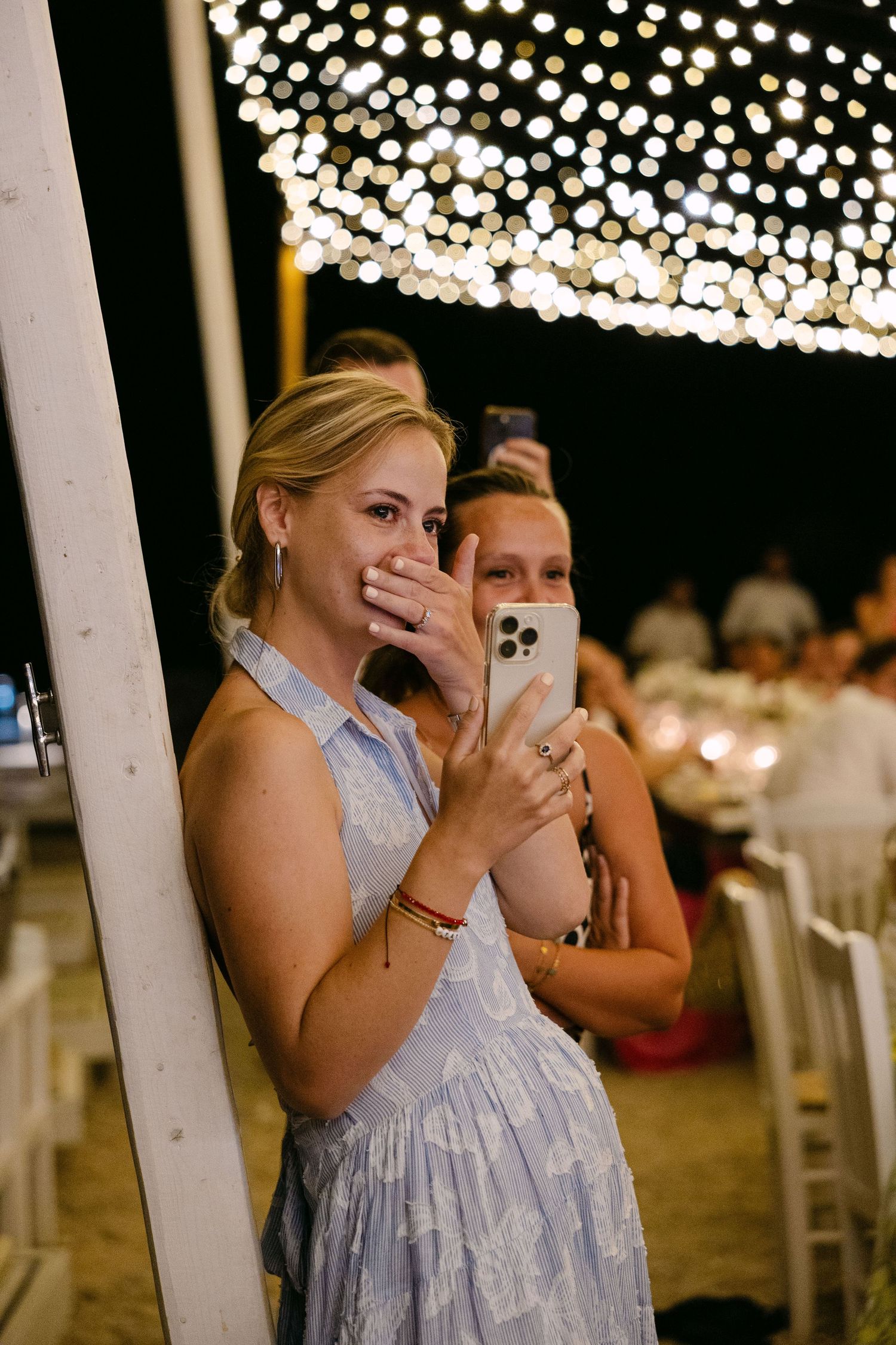 a wedding guest being visibly moved while holding her phone to record under carnival lights