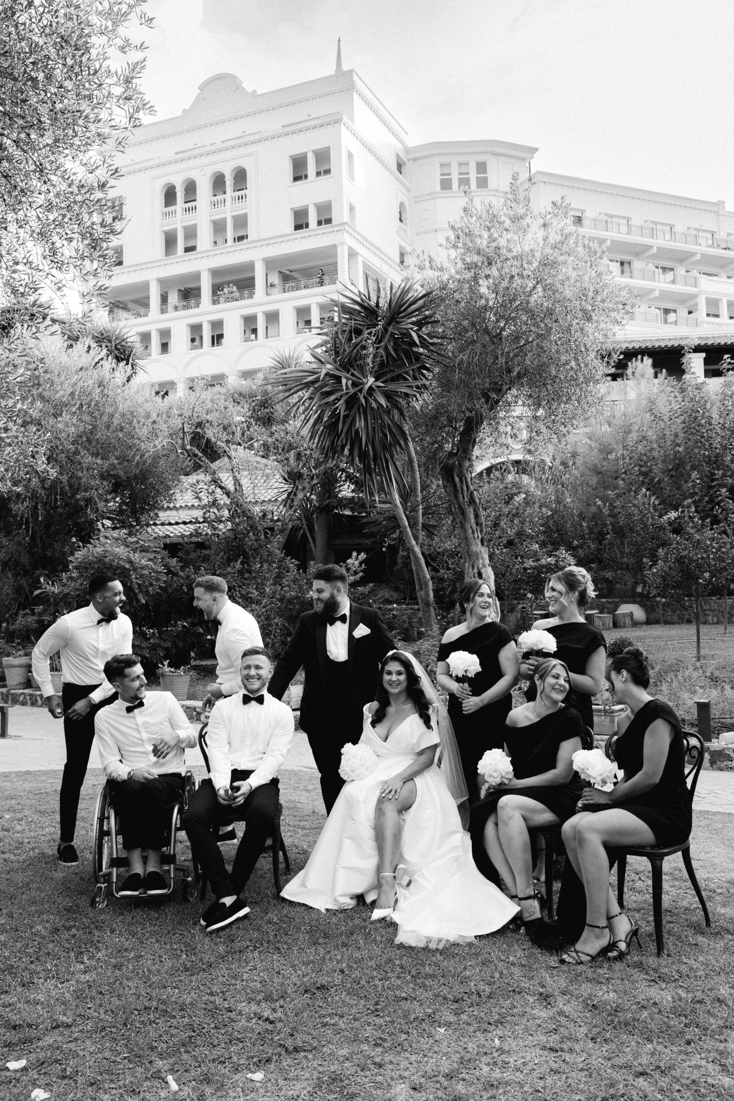 a black and white photo of a bridal and groom's party posing with the bride and groom for portraits, half of them sitting and smiling