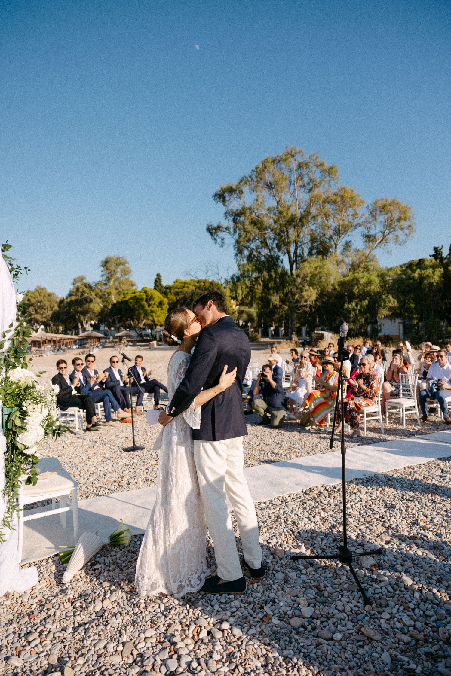 a bride and groom kissing while guests are seen in the backgound cheering