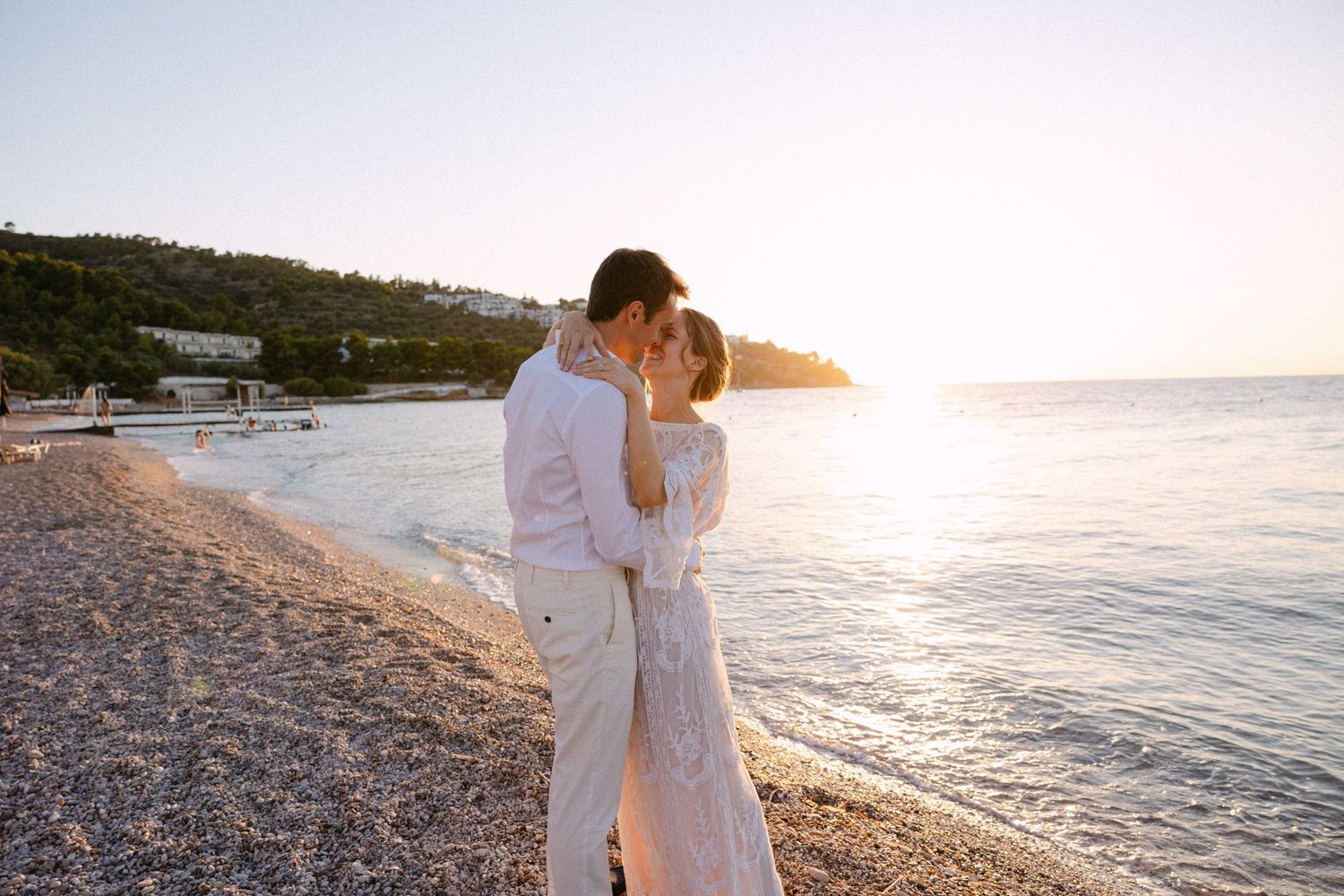 a bride and groom kissing in a greek beach at sunset