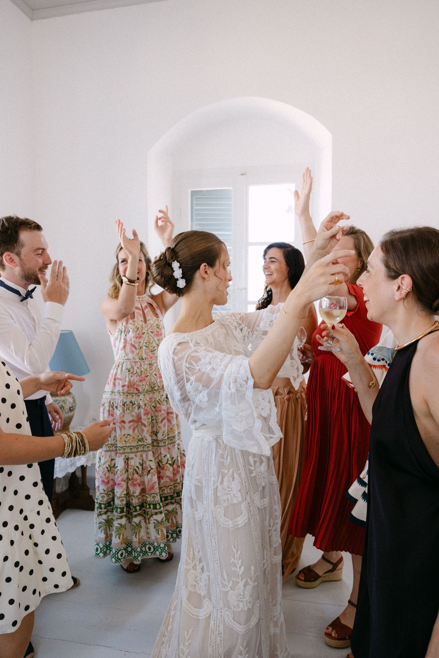 a bride celebrating with her friends in an indoor white setting during her getting ready - they are standing up and dancing laughing