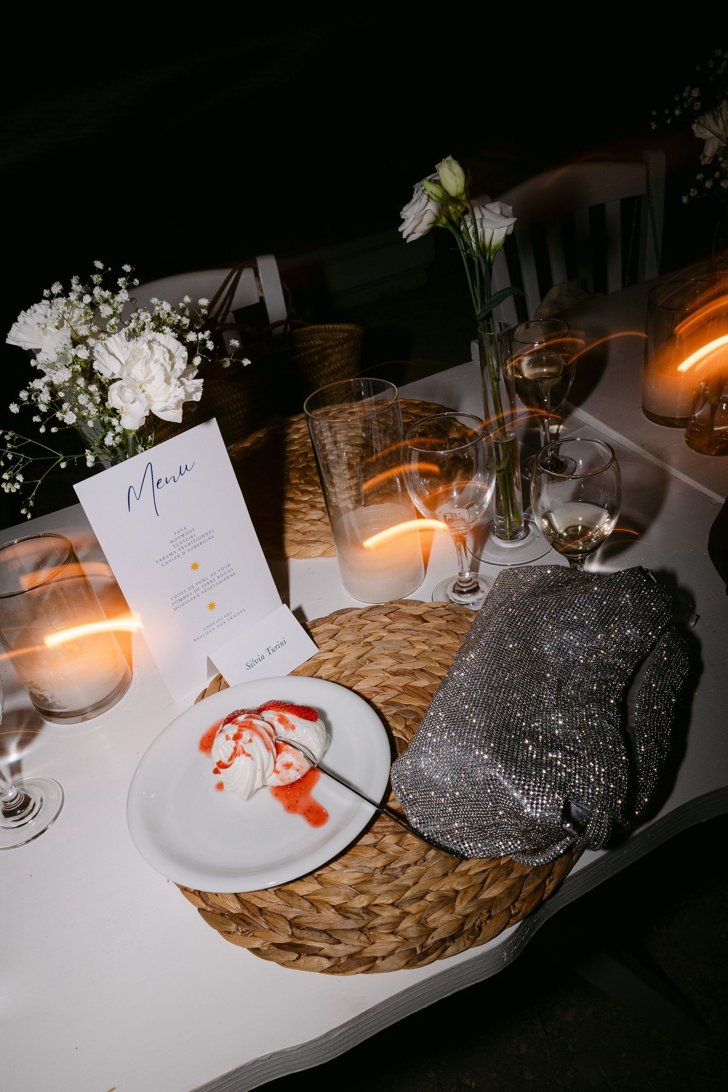 dinner table wedding details showing a cake, flower decorations, drinks, a handbag