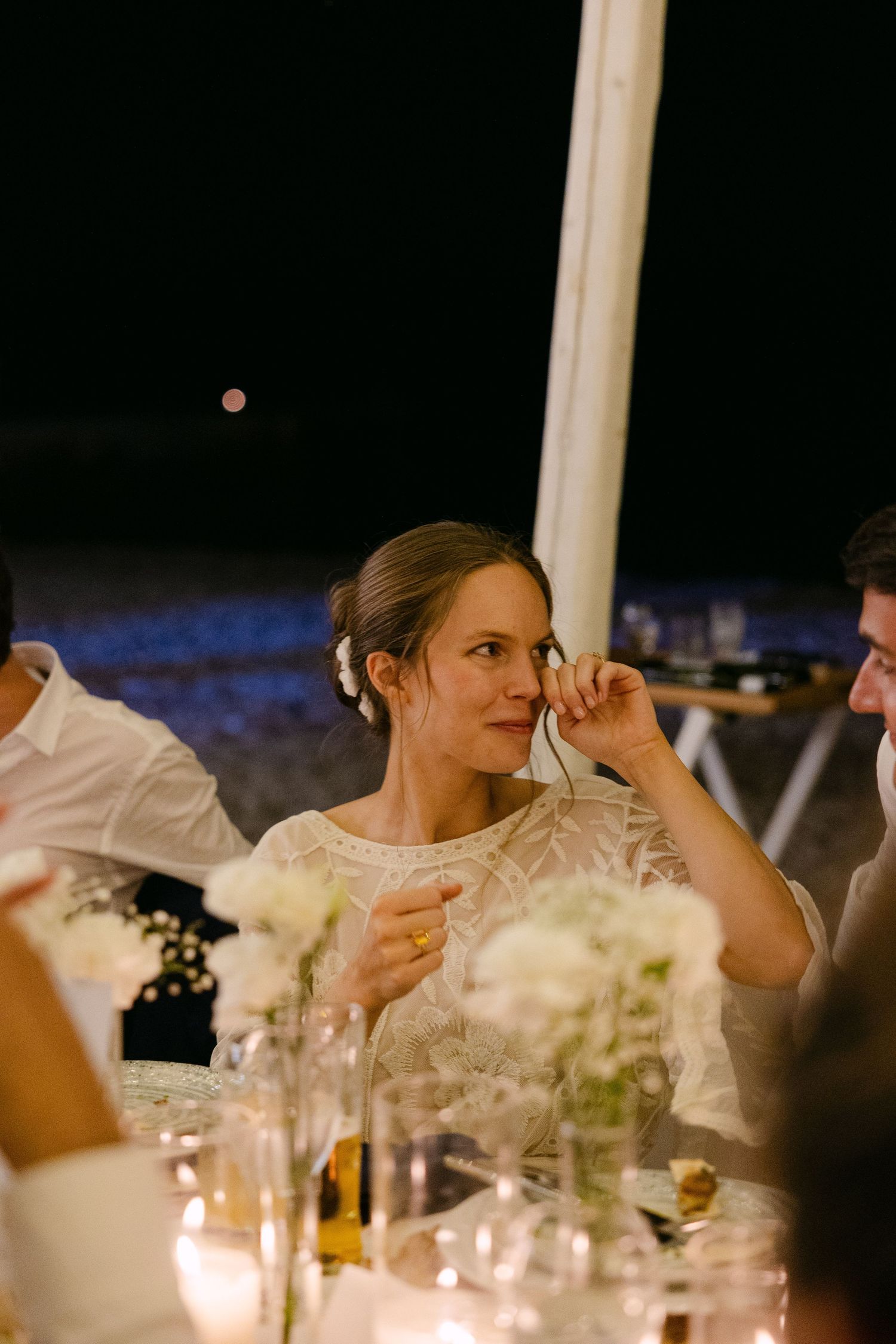 a crying bride wiping a tear and looking at her husband on their wedding table