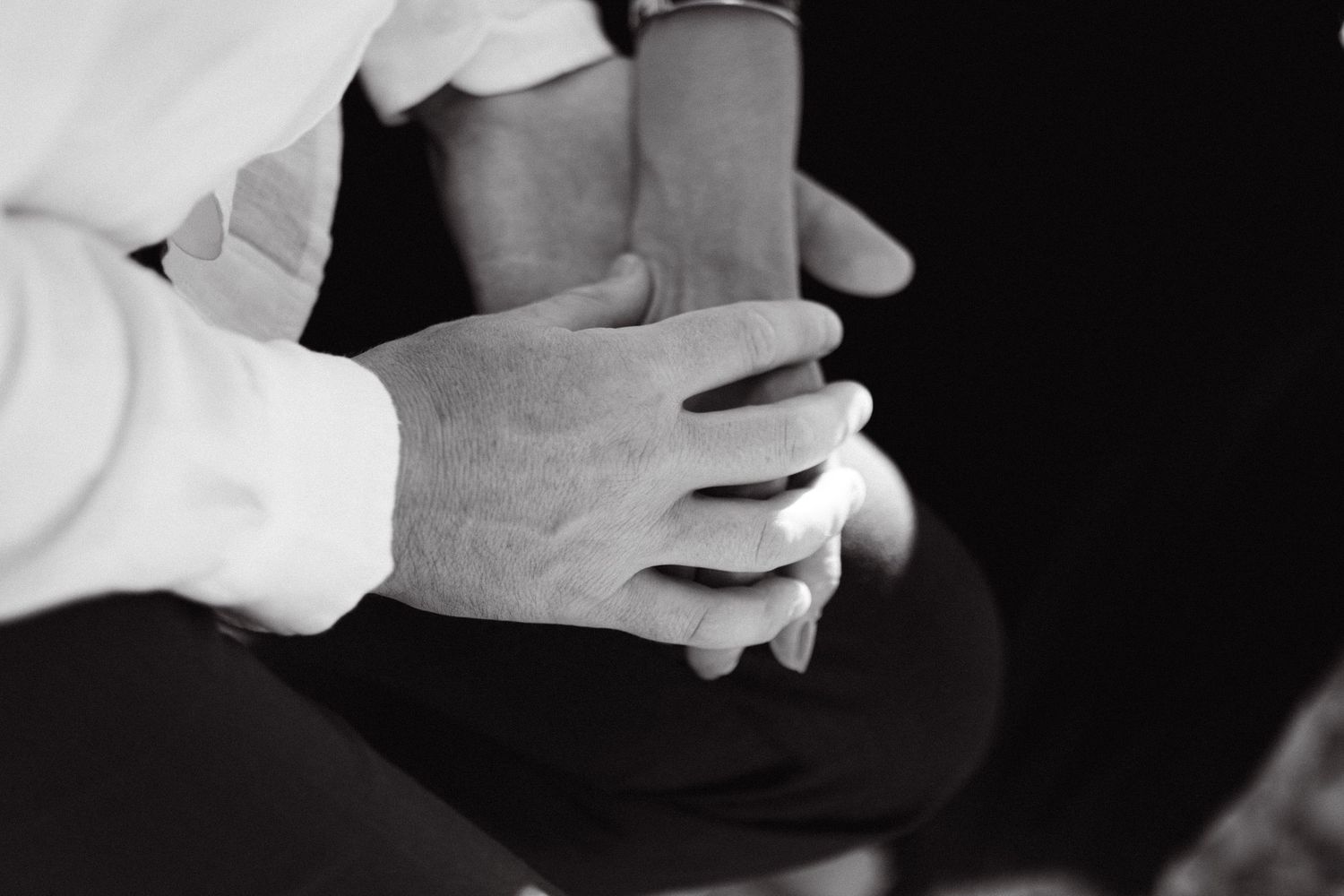 a black and white close-up photo of holding hands against a black background
