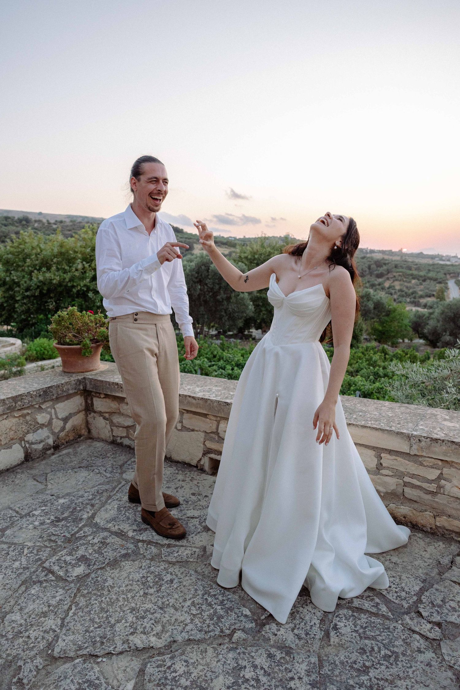 a bride and groom laughing candidly in an outdoors setting while the sun is setting behind them