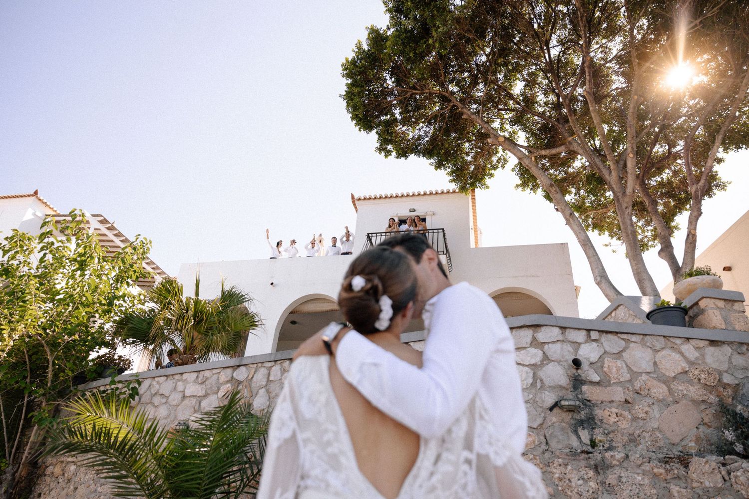 a wide photo showing an out-of-focus couple kissing where people are seen cheering in the background who are located inside a house