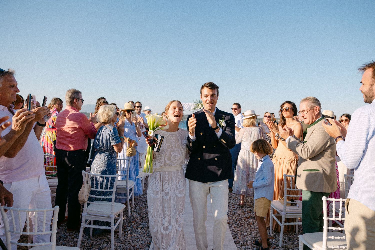 a bride and groom exiting their open-air beach wedding ceremony through the middle of the aisle while the guests are cheering