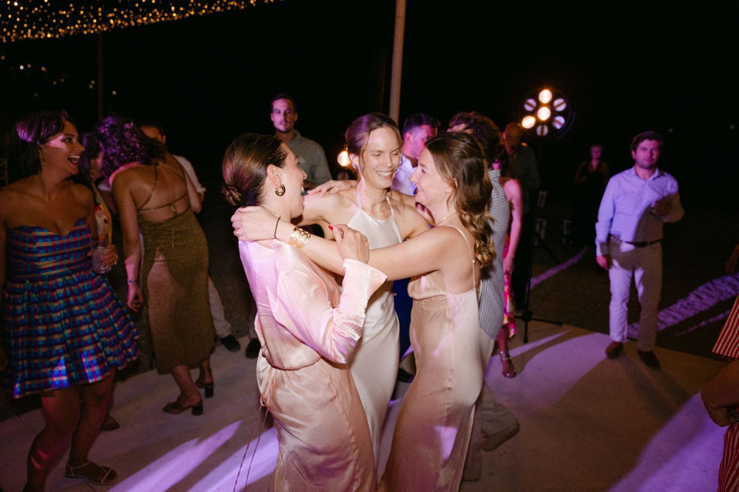 the bride and her two friends dancing and smiling during a summer wedding party in spetses, Greece