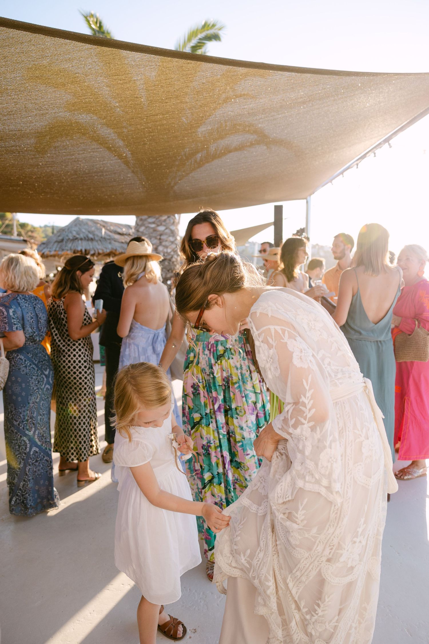 a little girl touch the bride's wedding dress together with the bride during sunset