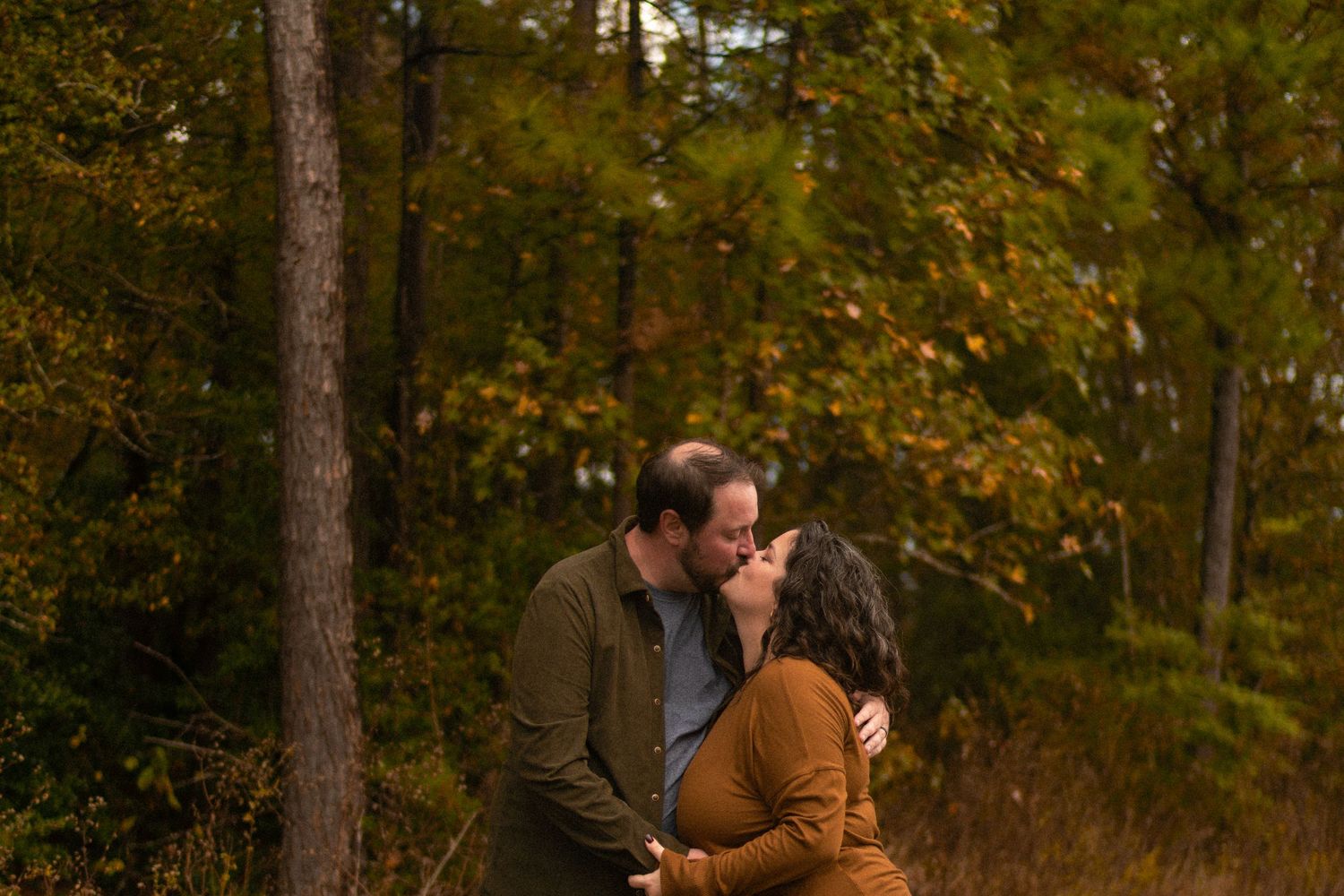 Couple sharing a tender kiss surrounded by colorful autumn foliage in a forest setting.