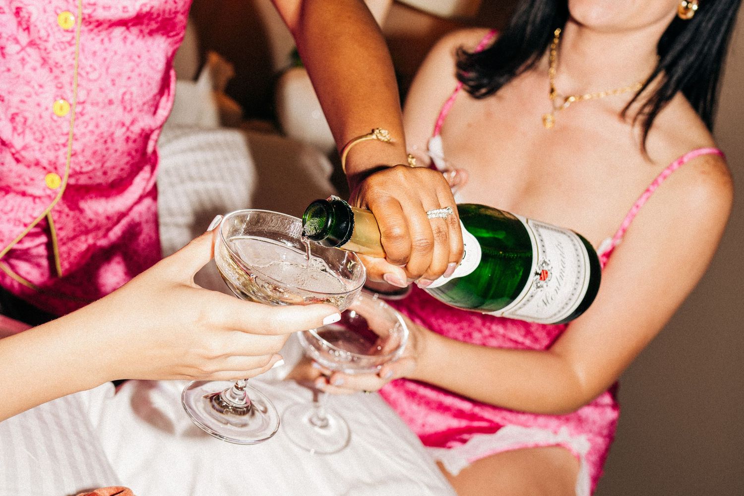 Women pouring champagne into glasses at a celebration, wearing pink outfits at a festive gathering.