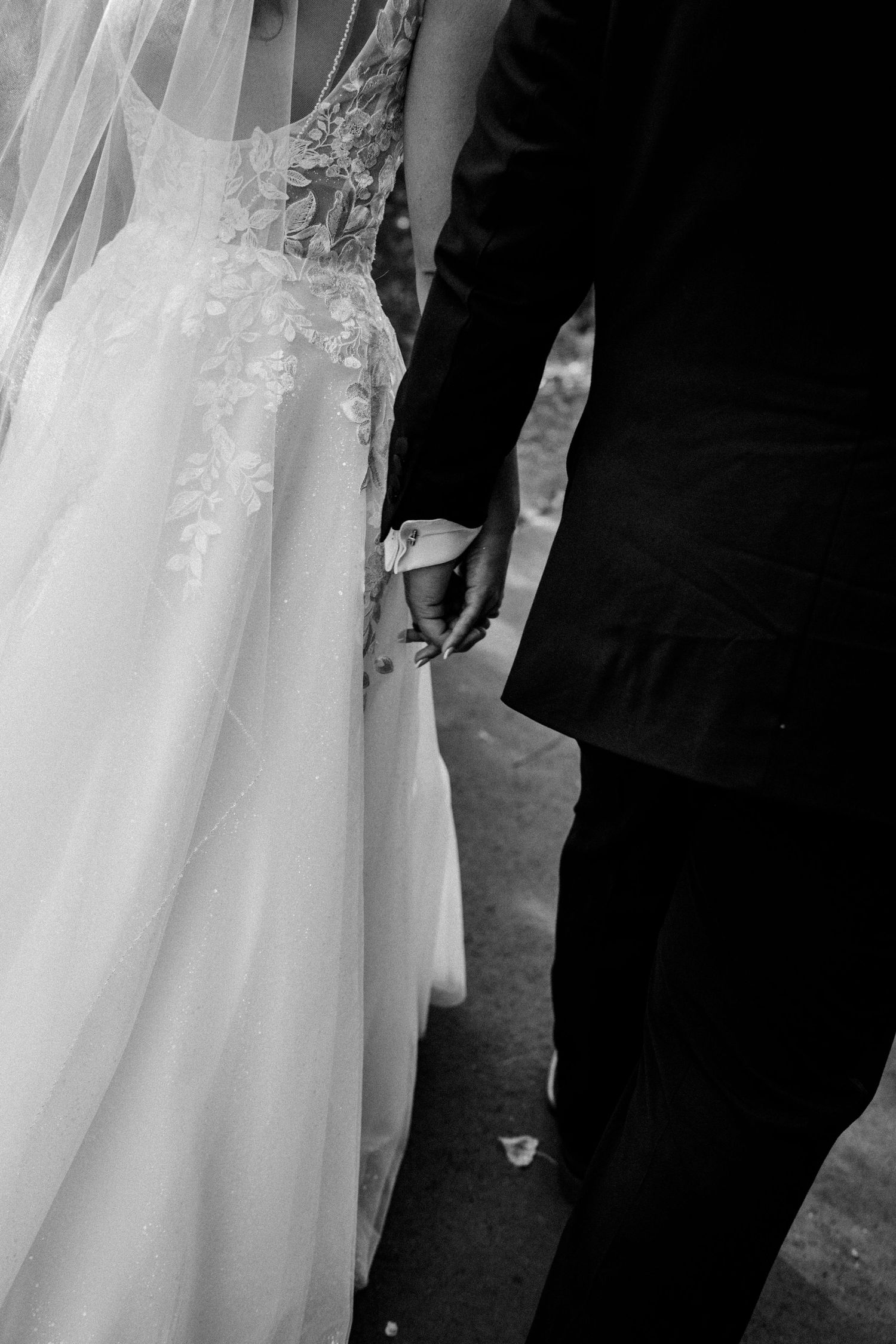 Black and white close-up of bride and groom holding hands, showcasing lace wedding gown.