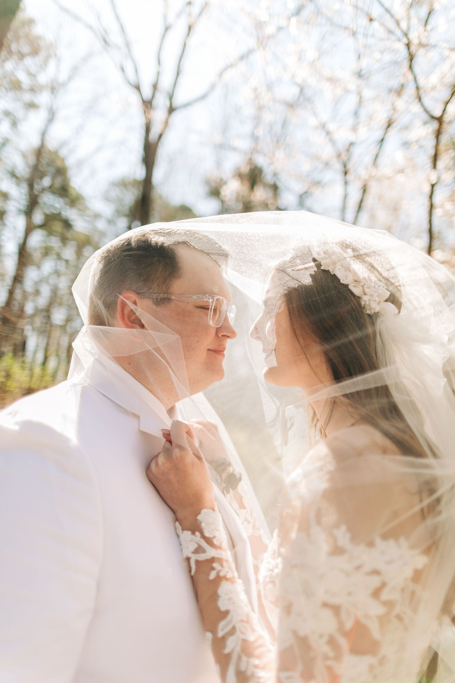 Bride and groom sharing an intimate moment under a lace wedding veil in a sunlit forest.