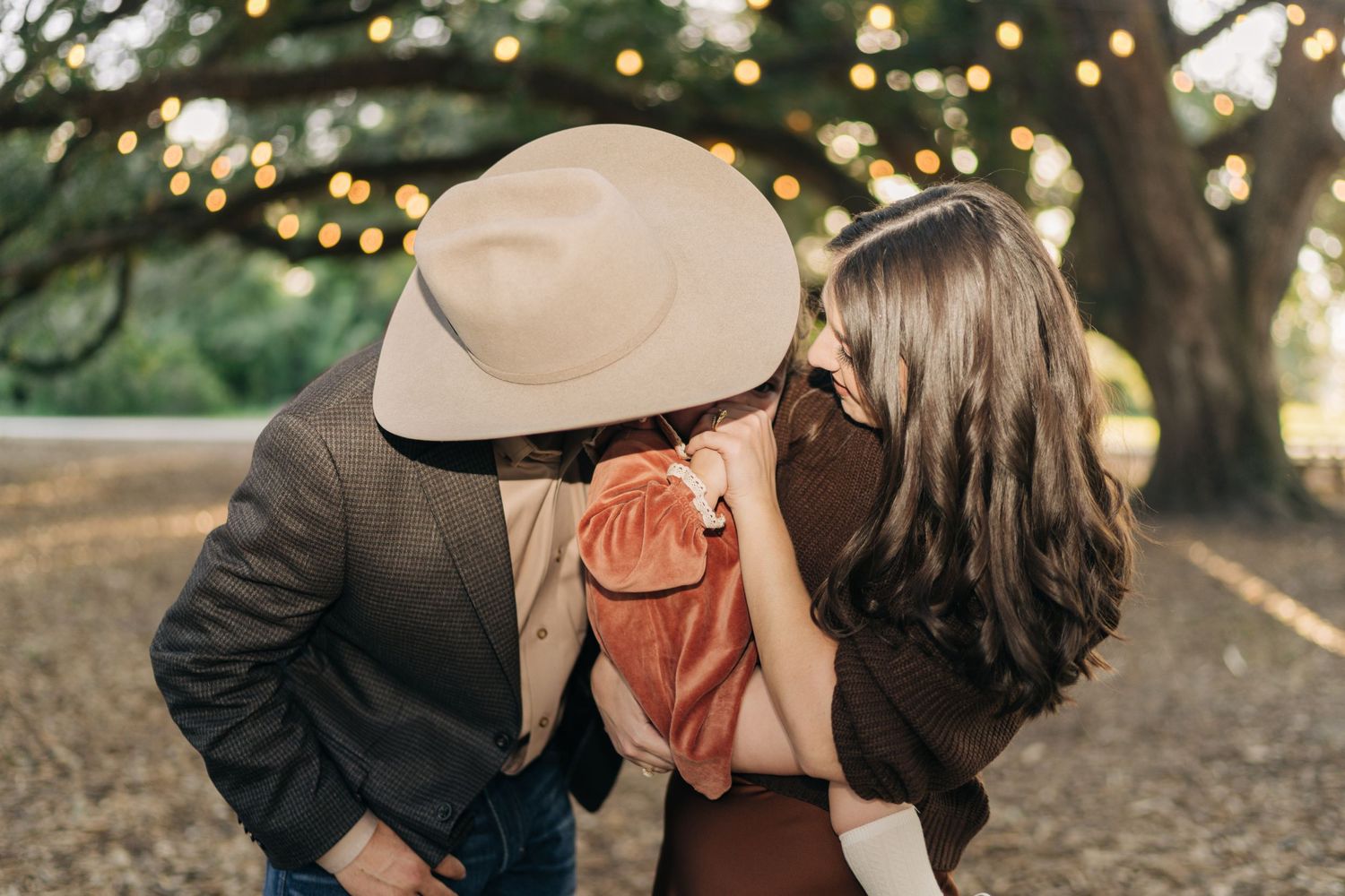 Couple sharing a romantic kiss under a tree adorned with warm fairy lights at golden hour.