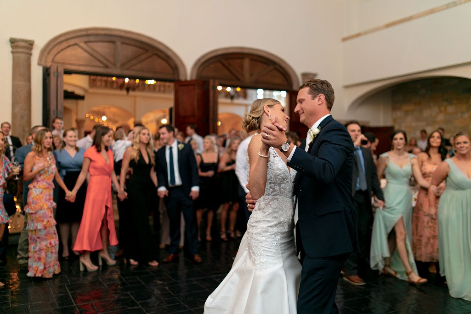 Bride and groom share their first dance at elegant wedding reception while guests watch and celebrate in the background.