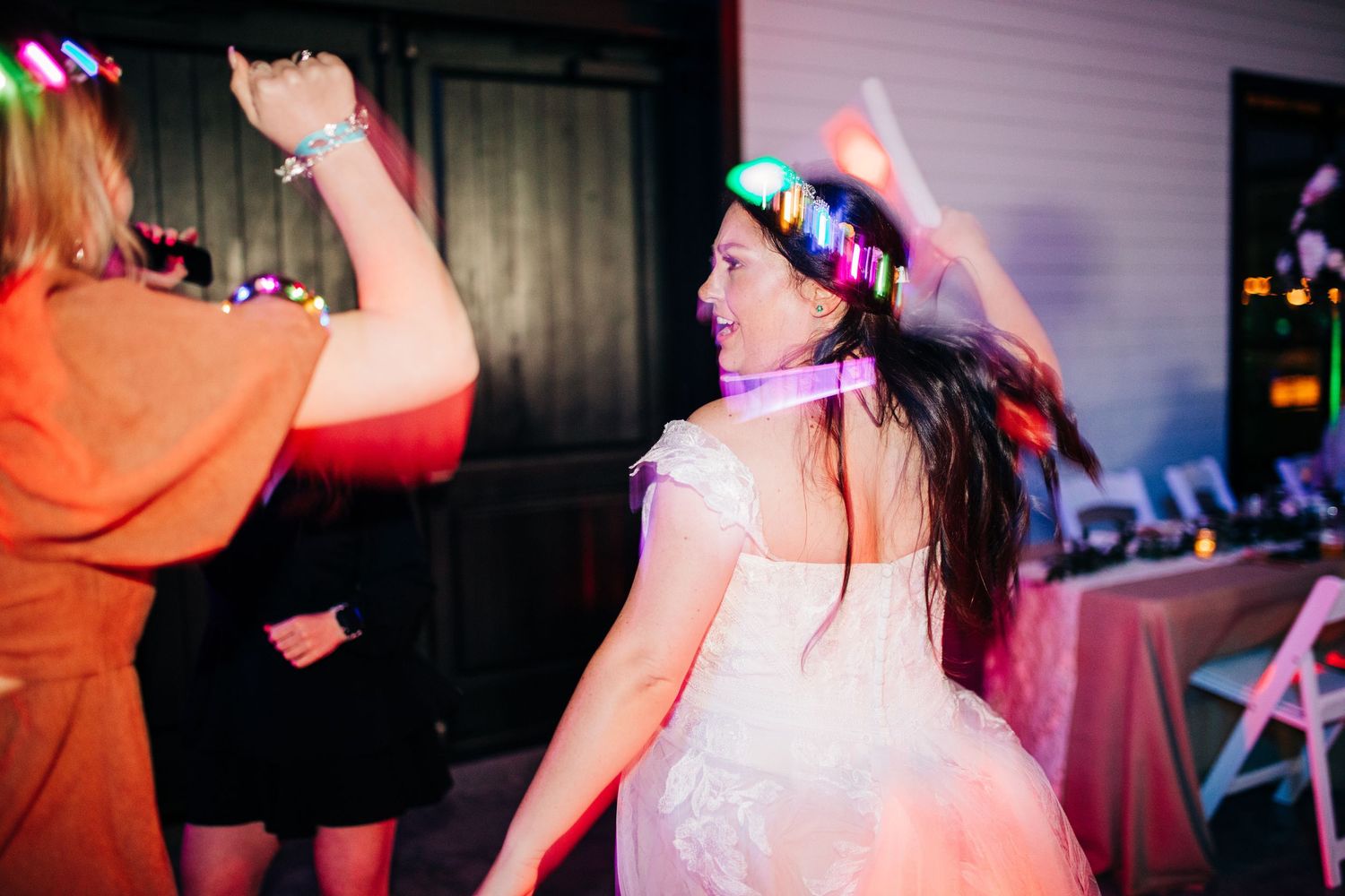 Bride dancing with glowing LED flower crown and neon accessories at a festive wedding reception.