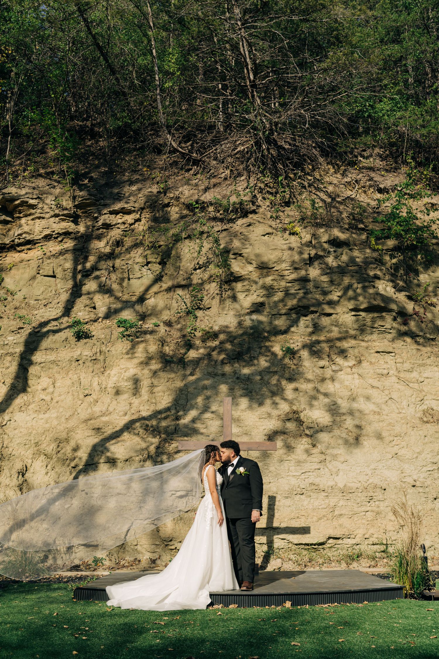 Bride and groom sharing a romantic moment against a dramatic sandstone cliff with tree shadows.