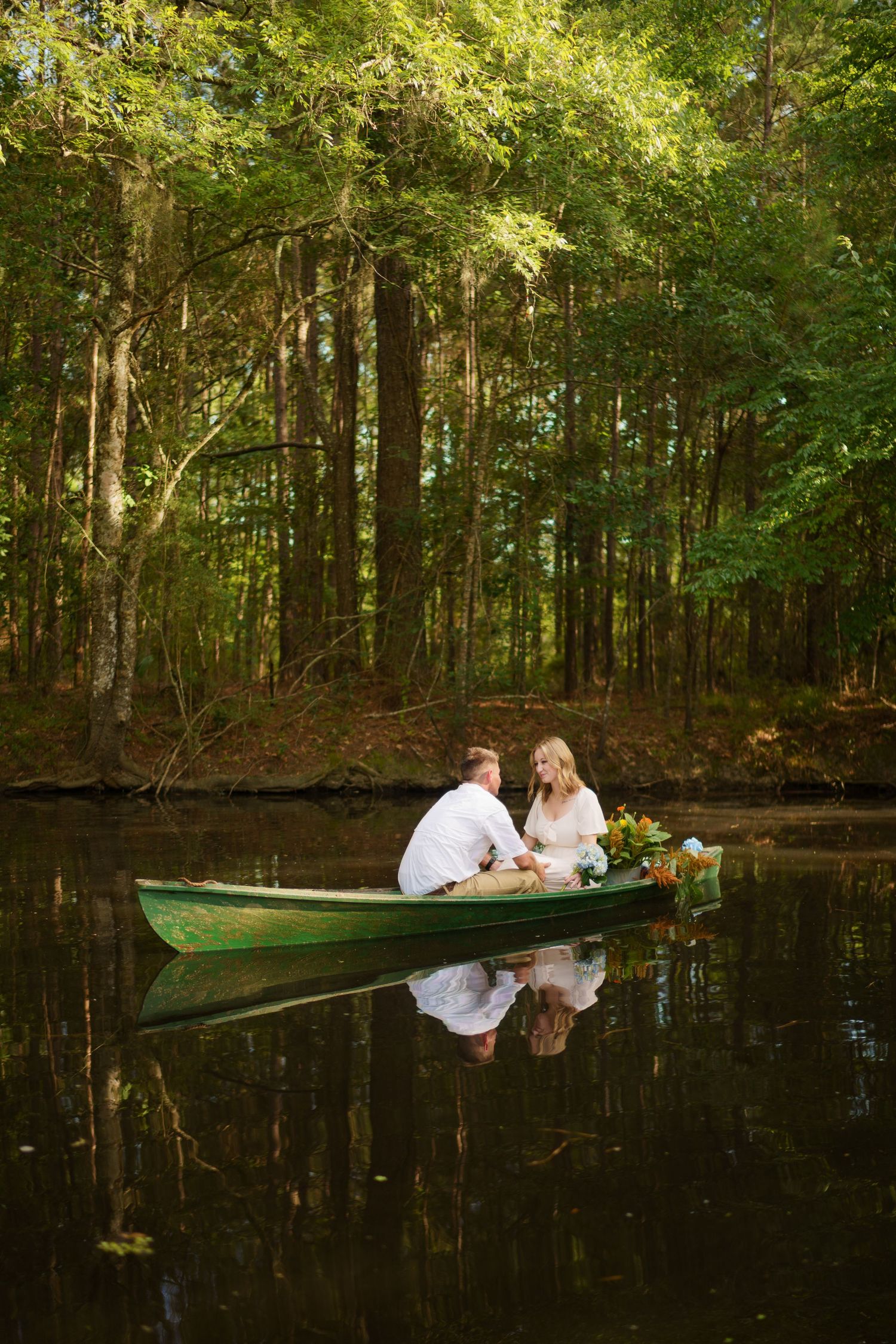 Couple sitting together in a green canoe on a calm reflective lake surrounded by lush green forest.