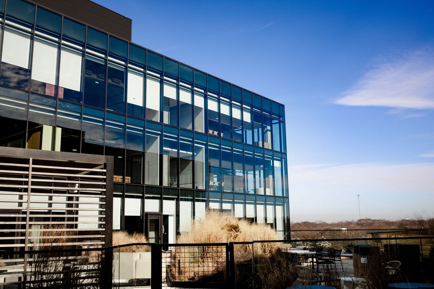 Modern glass office building with horizontal metal sunshades against bright blue sky on sunny day.