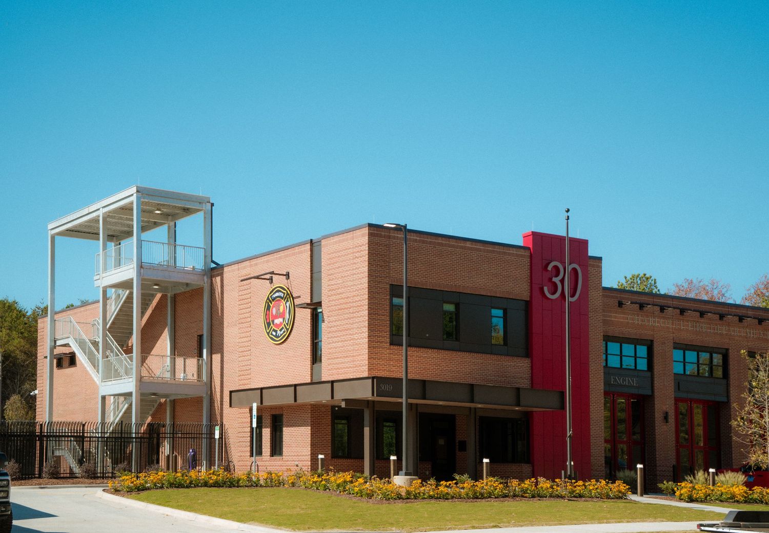 Modern brick school building exterior with glass entrance and pink accent walls under bright blue sky.