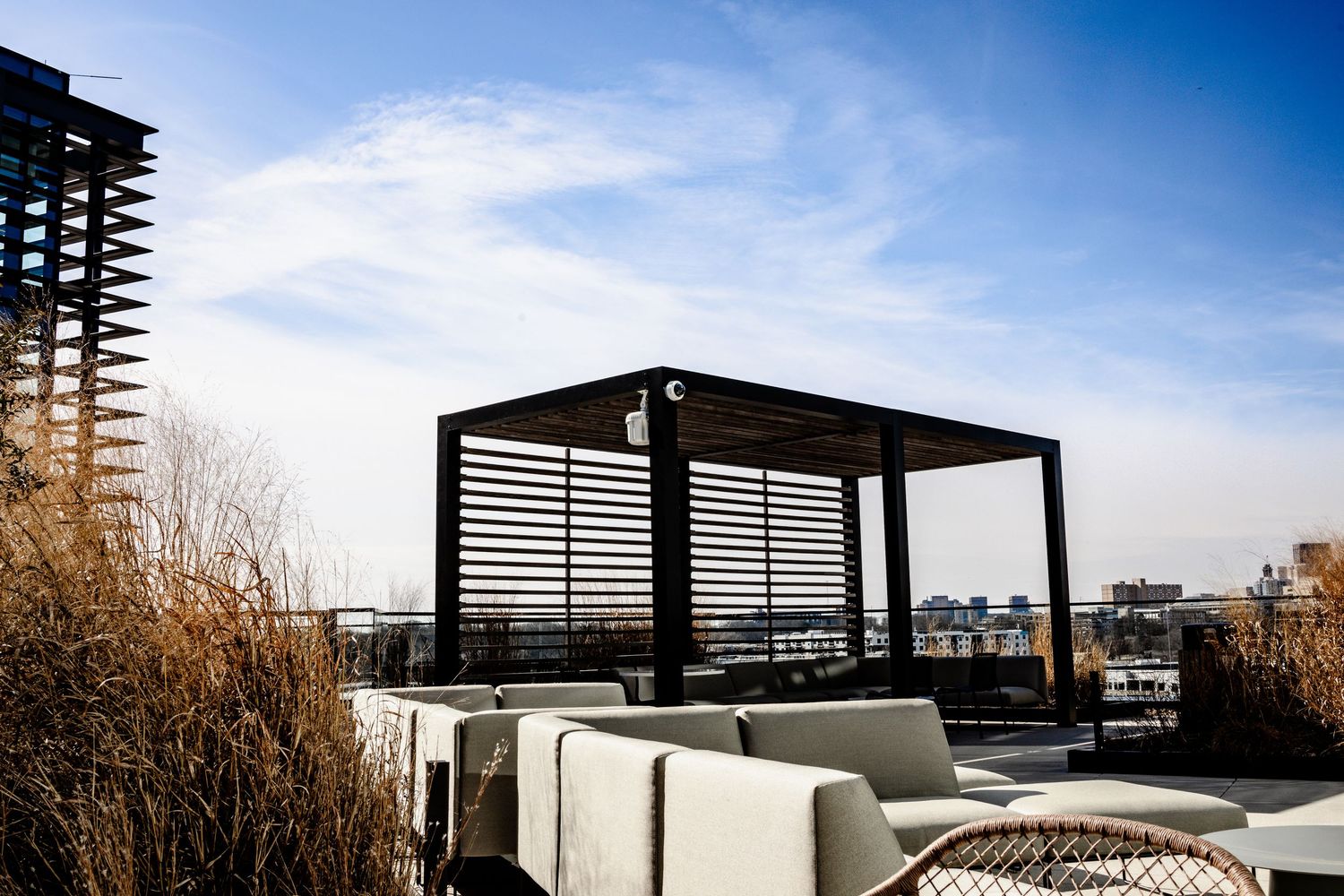 Modern rooftop terrace with horizontal slat railings and seating areas against an urban skyline on a sunny day.