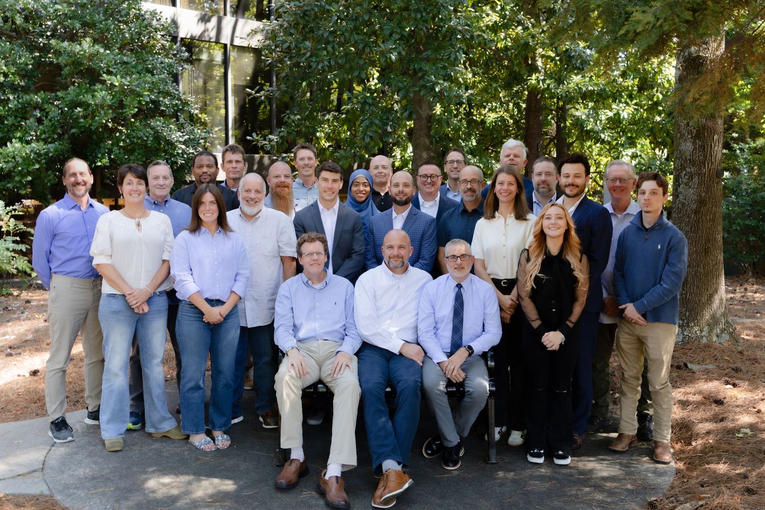 Large group photo taken outdoors under trees on sunny day.