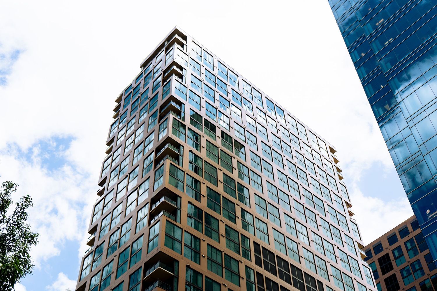 Modern glass and steel high-rise building reflecting blue sky and clouds in an urban downtown setting.
