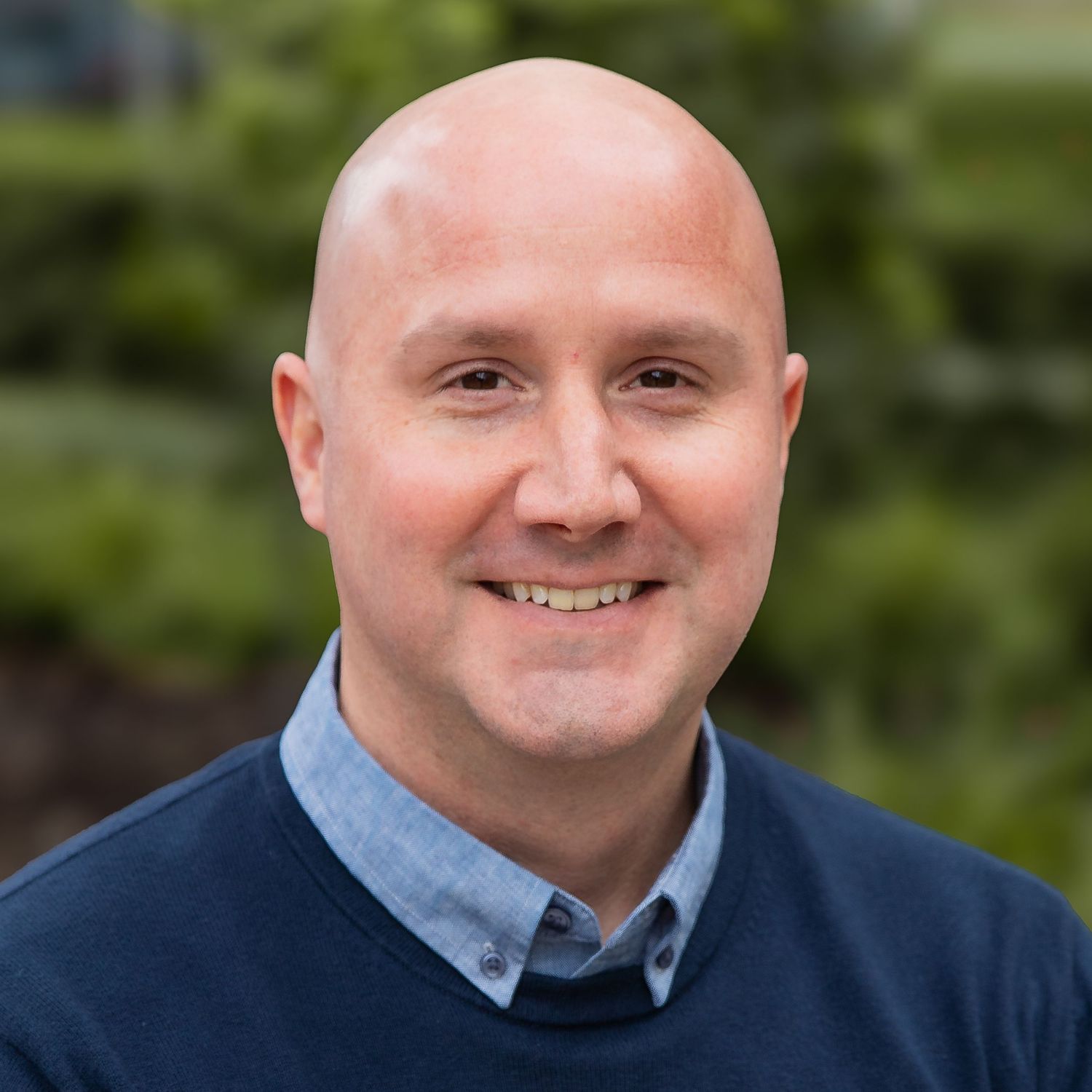 Four headshots showing expressions ranging from neutral to smiling, wearing a blue shirt and navy sweater.