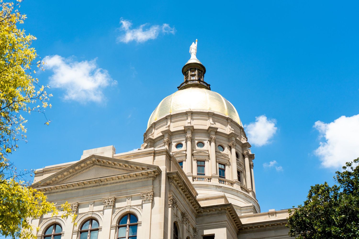 Classical government building with white dome and columns against bright blue sky with puffy clouds.