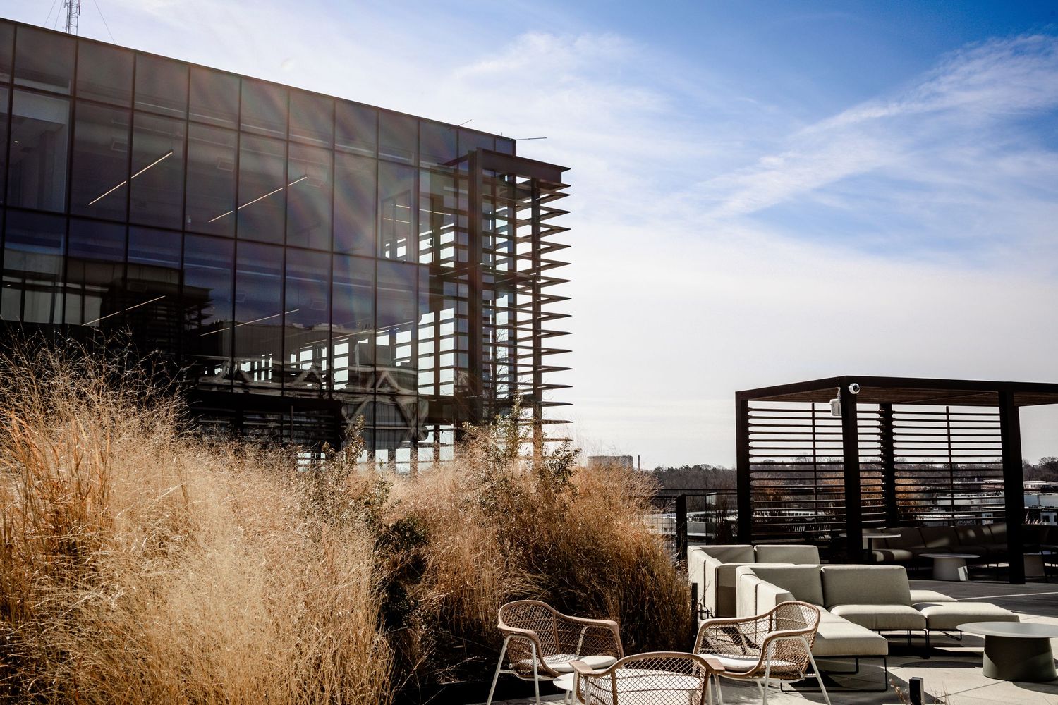 Modern glass building exterior with horizontal slats and reflective windows against a bright blue sky.