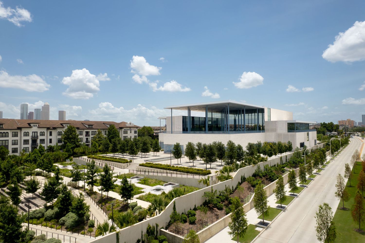 Aerial view of a modern museum building surrounded by manicured gardens and tree-lined paths in an urban setting.