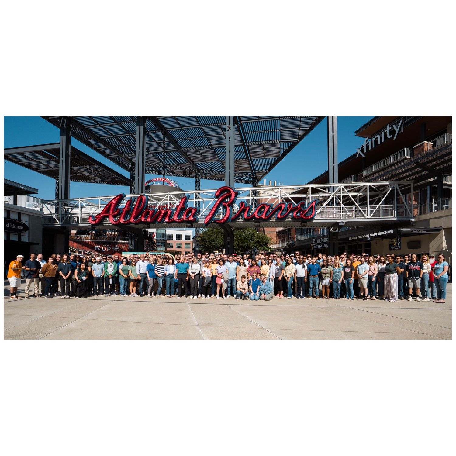 Large group photo of people posing in front of the Atlanta Braves stadium sign at Truist Park on a sunny day.