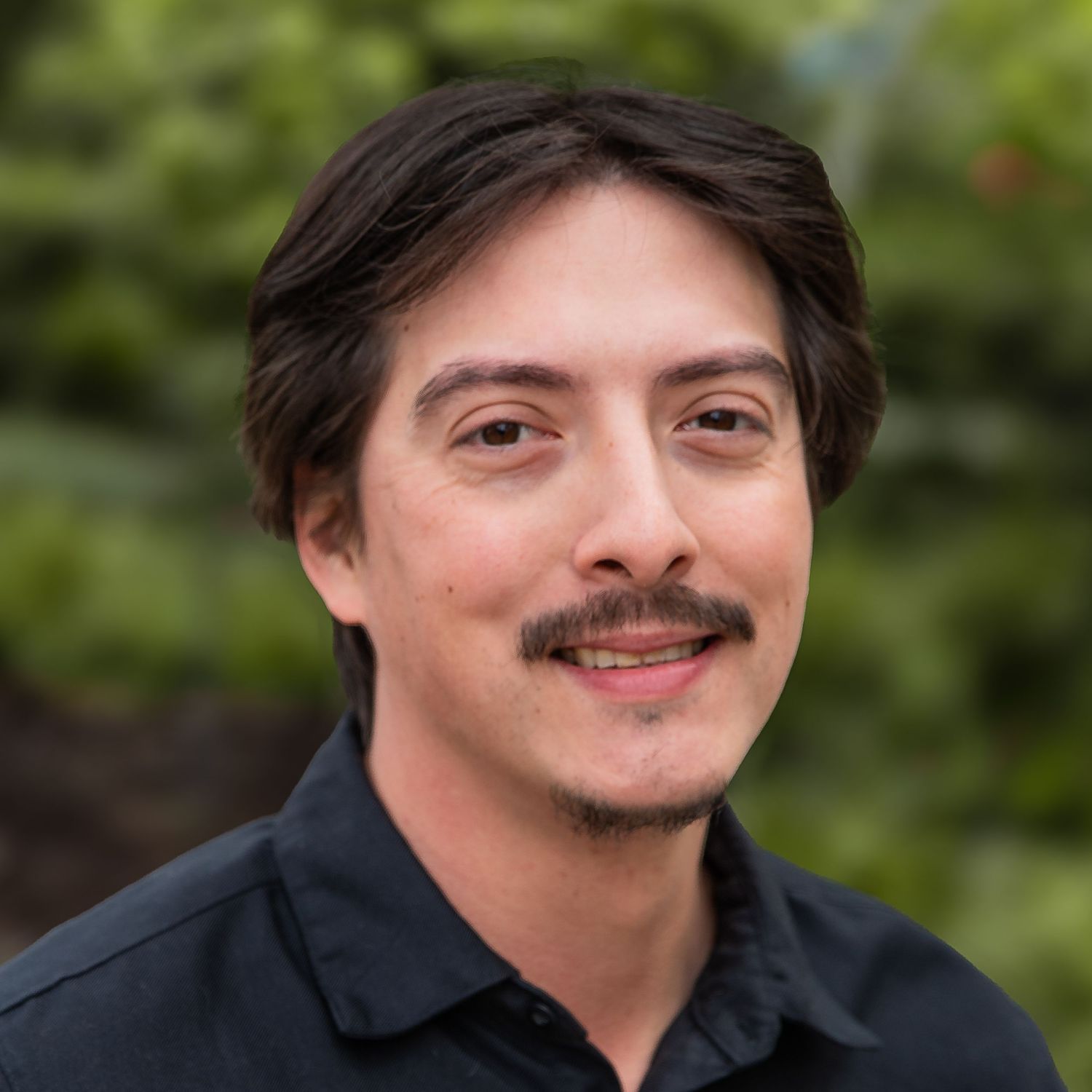 A person with a mustache and dark hair smiling at the camera in a sequence of close-up portrait shots.