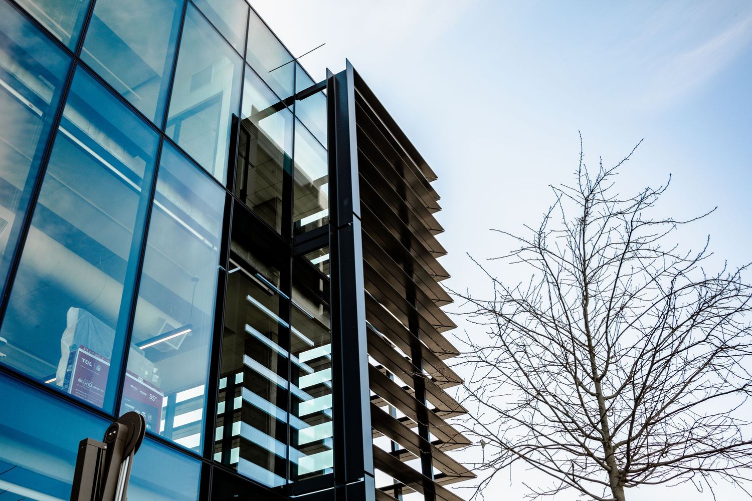 Modern apartment building with glass balconies and bare winter trees against a bright blue sky.