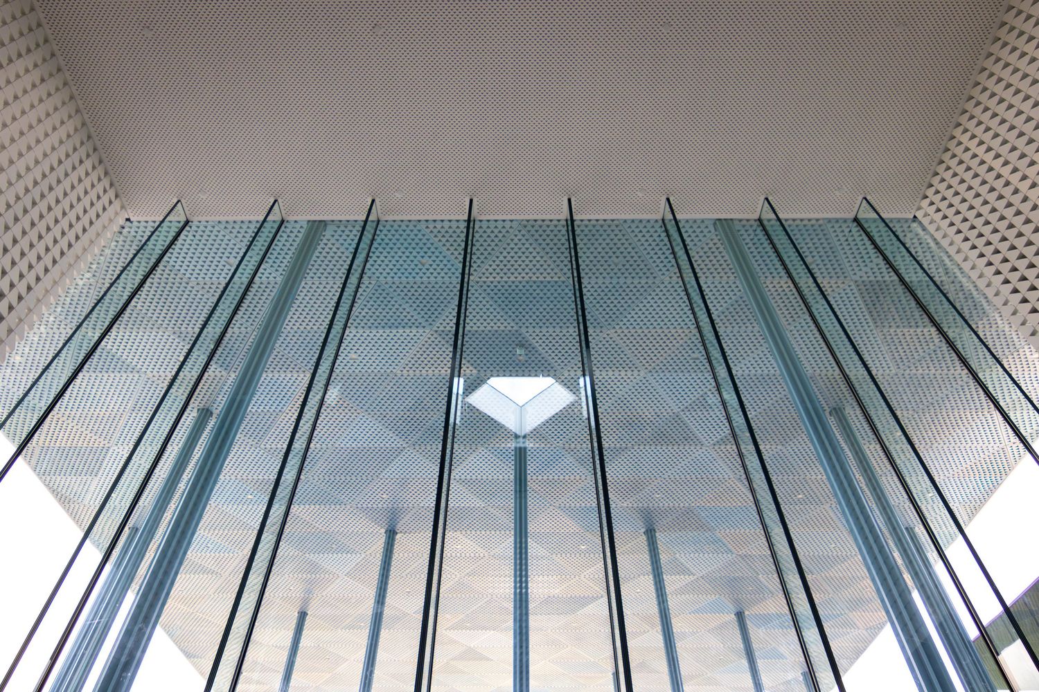 Modern glass ceiling architecture with geometric diamond pattern and vertical steel columns in contemporary building interior.