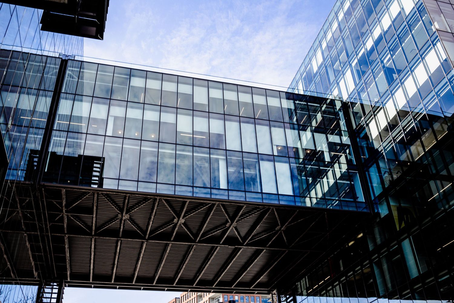 Modern office building with glass facade and connecting skybridge against blue sky.