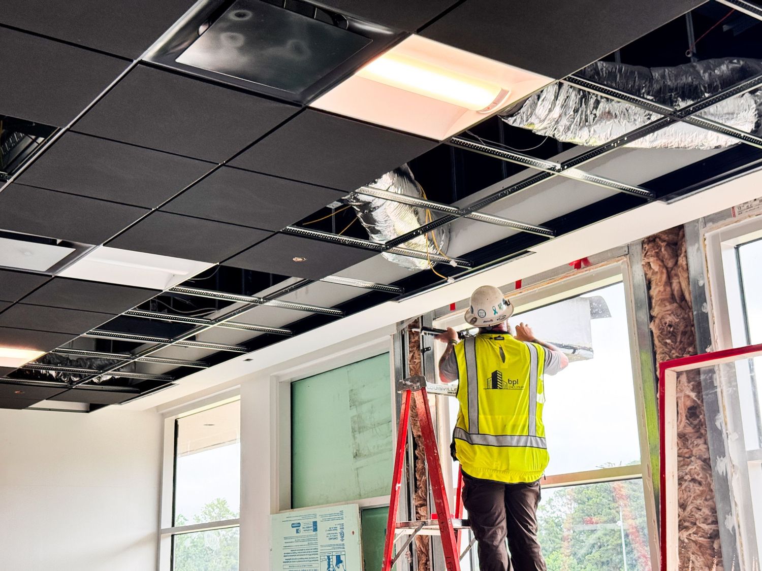 Workers installing new ceiling tiles and electrical components during commercial office renovation project.
