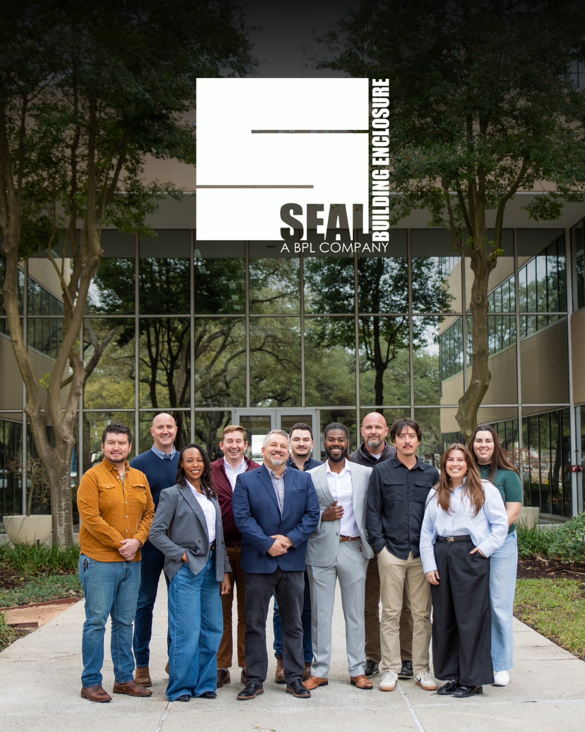 A group of business professionals standing together outside a modern office building with glass windows and trees.