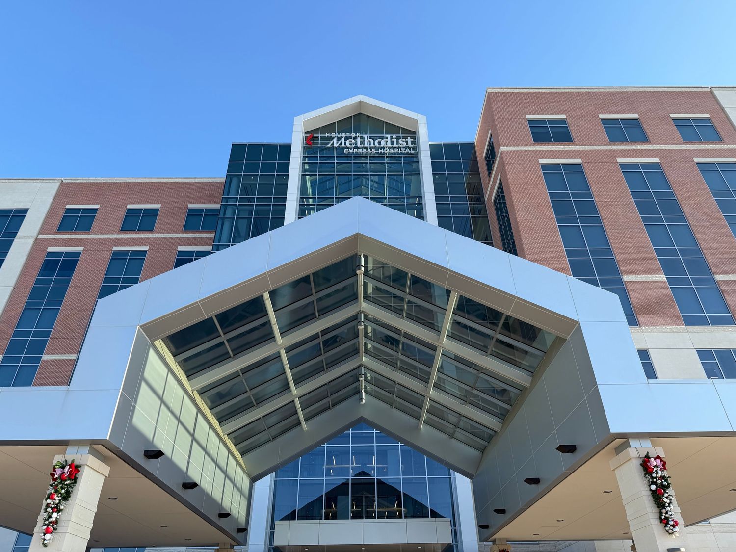 Methodist hospital building exterior with modern brick facade, large glass windows, and holiday wreaths under blue sky.