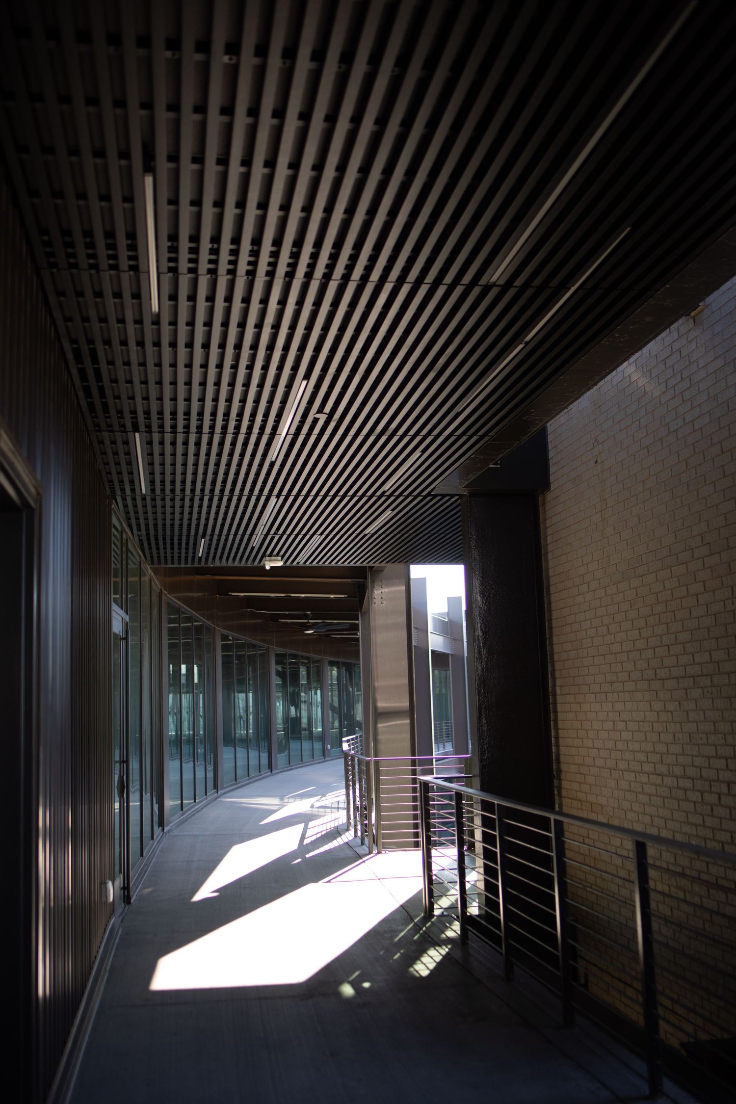 Long corridor with dramatic lighting and slatted ceiling design creating geometric shadows.