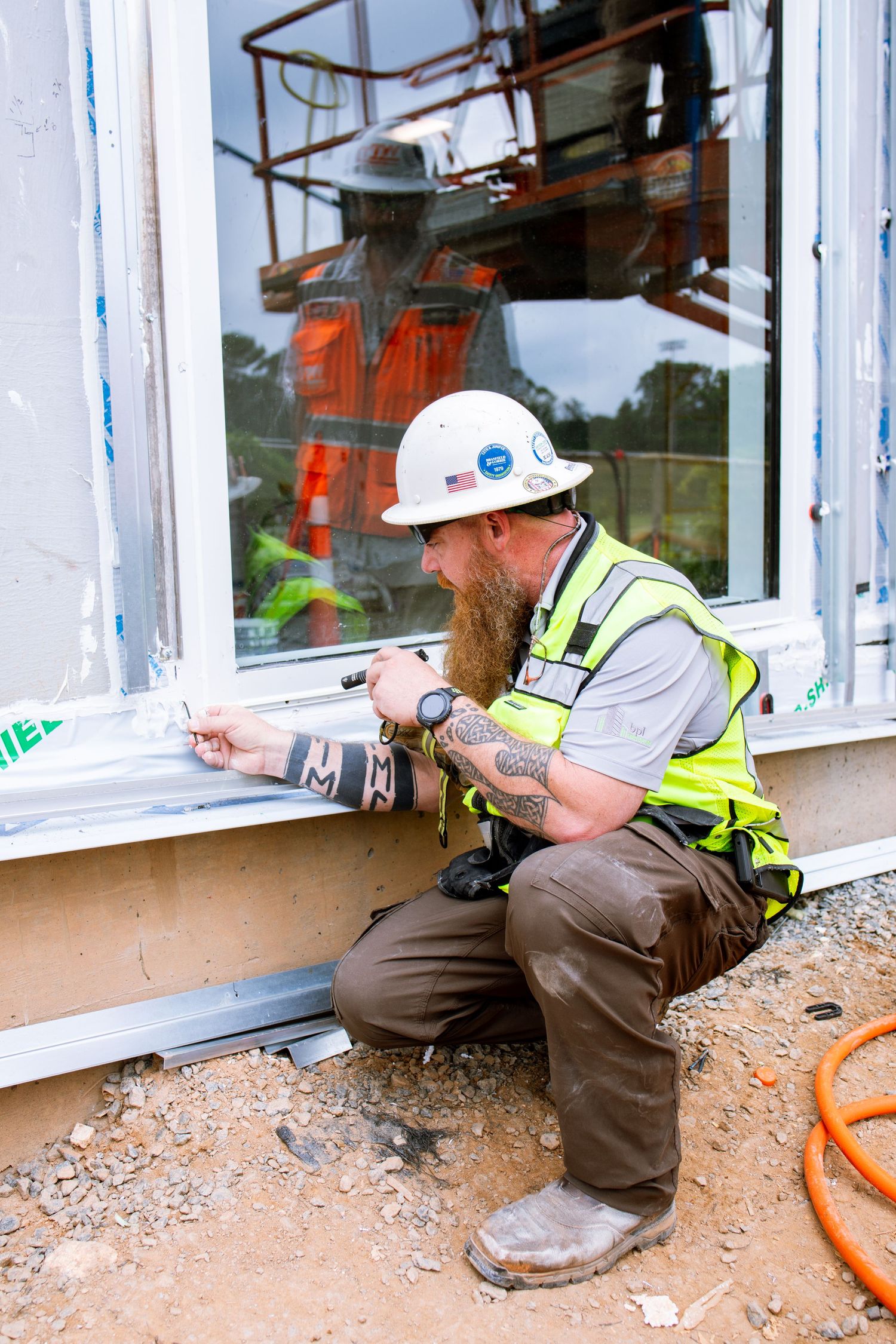 Worker in safety gear installing window components from an aerial lift platform.