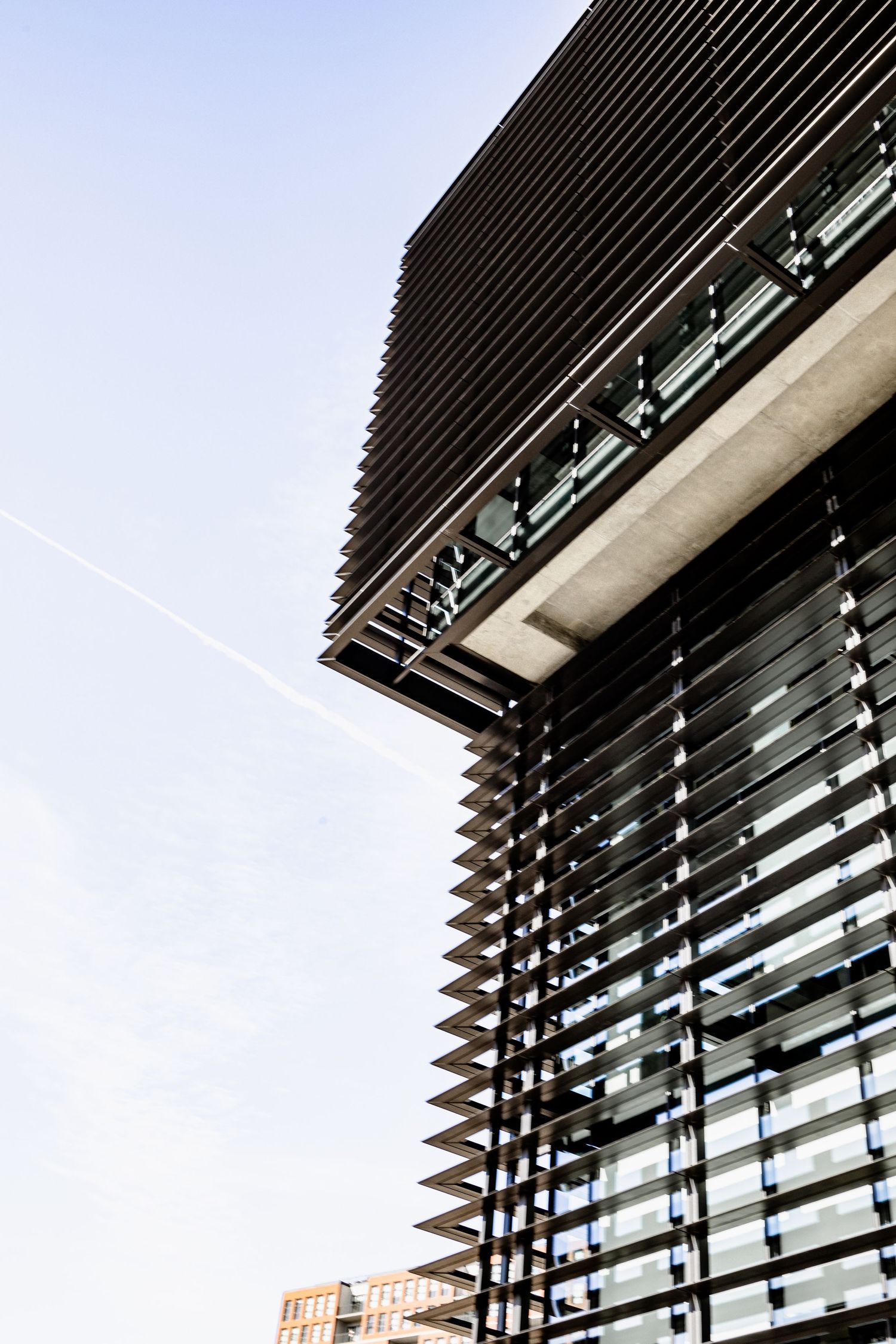 Modern office building exterior with angled horizontal metal louvers and glass windows creating geometric patterns against blue sky.