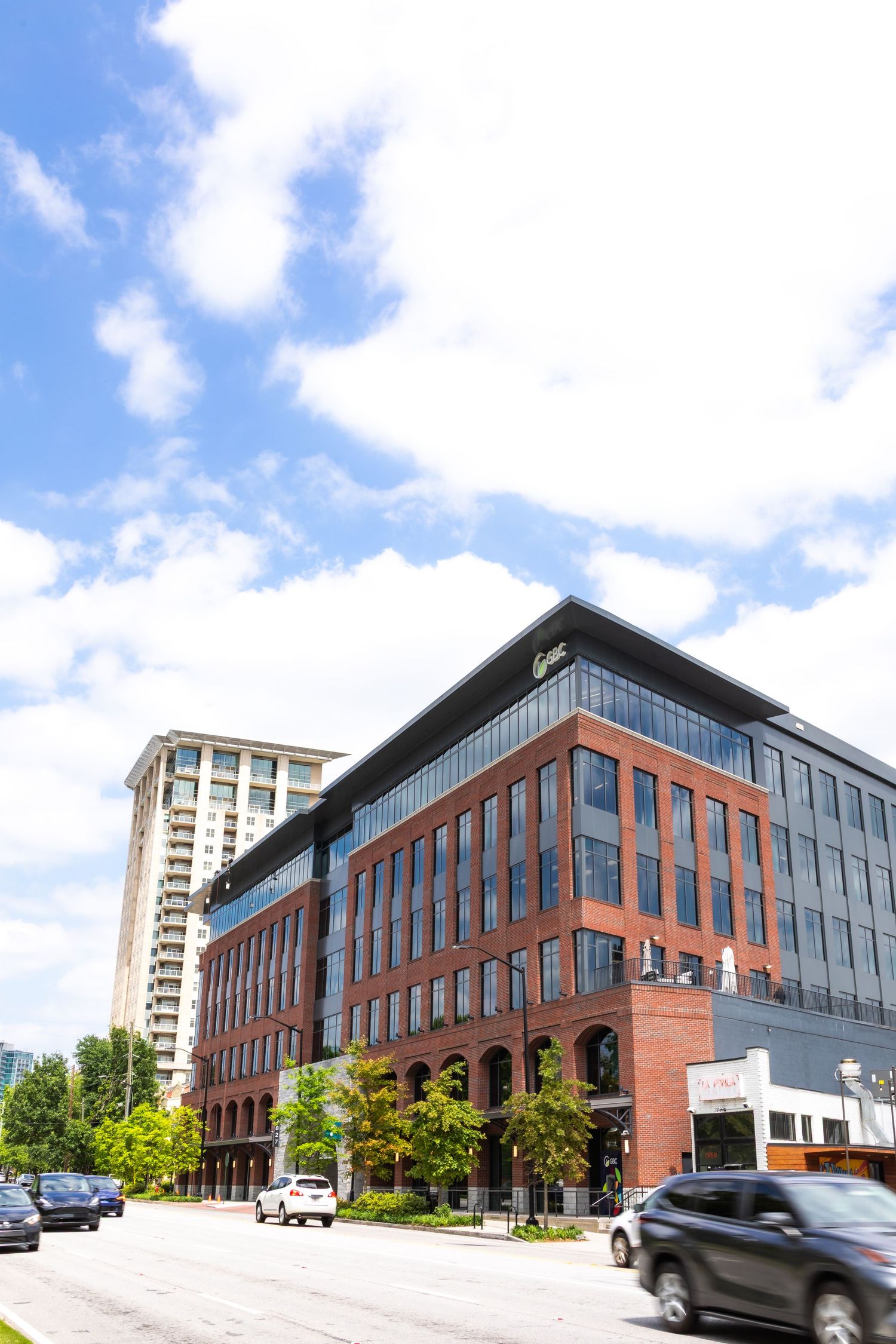 Modern brick and glass office building with curved architecture under blue sky with white clouds in urban setting.