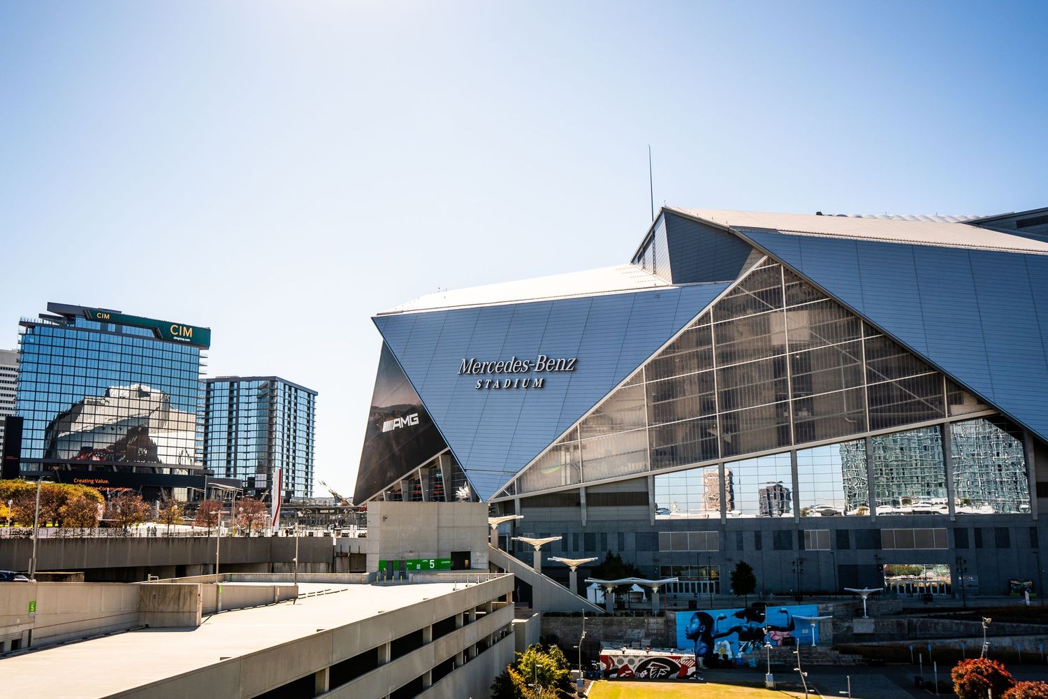 Modern stadium and entertainment complex buildings with glass and steel architecture against a bright blue sky.