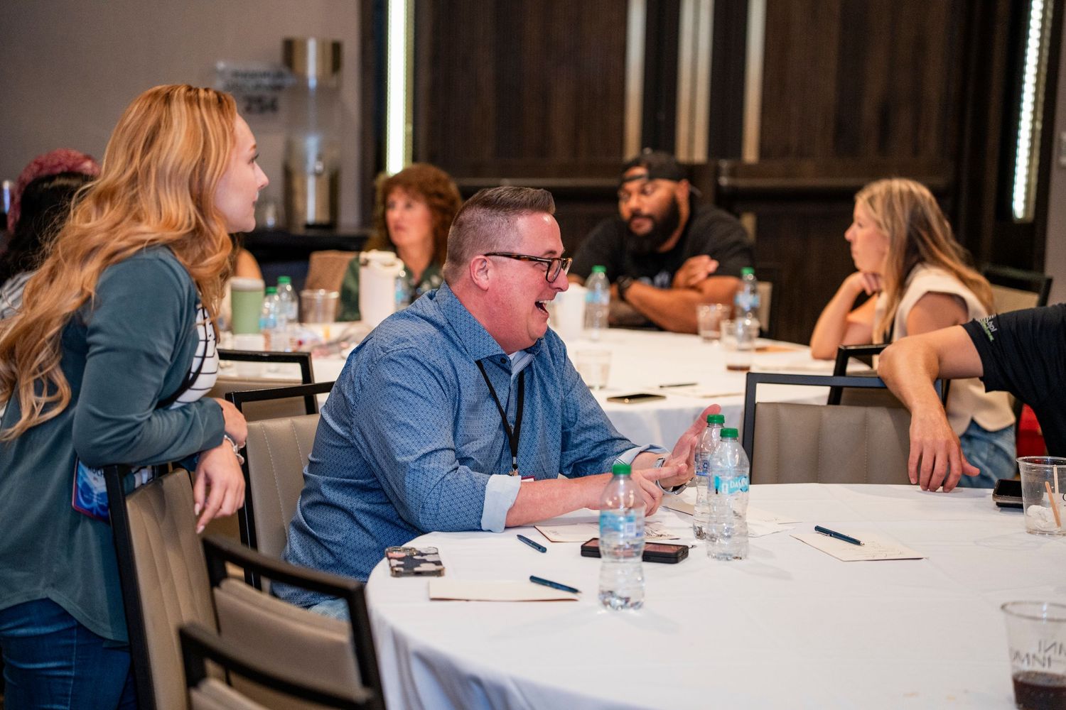 Business professionals collaborate during a workshop at round tables in a modern conference room setting.