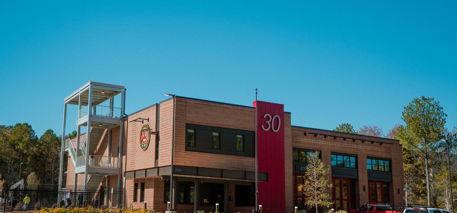 Modern brick commercial building with red accent wall and glass windows under bright blue sky.